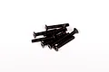 A small pile of black metal countersunk head screws with hex drive sockets, isolated on a white background.