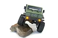 Matte green Hobby Plus CR-18P V3 T Hunter RC rock crawler climbing over a rock with illuminated yellow headlights.