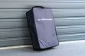 A black and grey Koswork carrying bag for 1/8 scale RC cars standing upright against a grey roller door.