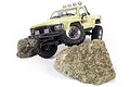 A creme-colored 1/18 scale HPI Venture18 RC Toyota Hilux SR5 rock crawler climbing over two large, textured rocks on a white background.
