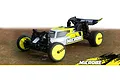 Maverick MiCROBE 1/24 scale RC buggy in yellow and white, featuring black wheels and a rear wing, positioned on a textured brown surface.