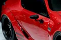 A close-up of a black side mirror mounted on a red 1/10 scale RC car body shell.