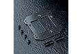 MST carbon fibre battery mount plate with four screws and two cylindrical metal posts on a dark textured background.
