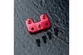 A red anodized aluminium steering arm mount for an RC car, accompanied by four black flat-head screws on a dark textured surface.