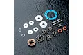 A set of MST limited slip differential parts including metal gears, washers, pins, O-rings, and a blue gasket on a dark textured surface.