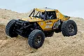 UDI UCX24 Snow Leopard 1/24 scale yellow RC rock crawler parked on sandy terrain outdoors.