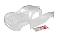 A clear, unpainted polycarbonate body shell for the Traxxas Unlimited Desert Racer RC truck, shown with an included sheet of Traxxas logo decals.