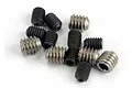 A collection of twelve small metal grub screws, some black and some silver, scattered on a white background.