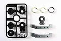Tamiya RC servo mount and servo saver parts including a black plastic parts tree, two gunmetal aluminium mounts, and metal rings.