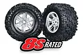 Two Traxxas X-Maxx monster truck wheels with aggressive tread tyres and satin chrome rims, featuring an 8S RATED logo overlay.