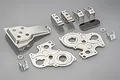 A collection of Tamiya Frog metal pressed chassis parts including gearbox plates, suspension mounts, and a small black plate on a grey background.