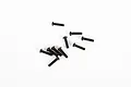 A collection of ten black button head screws scattered on a plain white background.