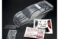 Traxxas Rustler clear unpainted polycarbonate RC body shell with included decal sheet, rear wing, and hardware bag on a black background.