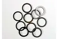 A collection of ten small, thin, dark grey PTFE-coated washers scattered on a white background.