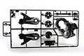 A black plastic Tamiya RC parts sprue containing suspension arms, gearbox components, and small mounts on a white background.