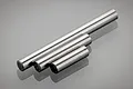 Three cylindrical metal gearbox shafts of varying lengths arranged diagonally on a reflective surface.