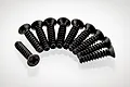 A set of ten black metal countersunk screws with coarse threads arranged in a semi-circle on a white background.
