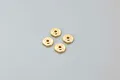 Four small, circular brass shock pistons for RC cars arranged in a square pattern on a plain light grey background.