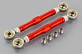 Two red anodized aluminium steering linkages with silver ball joints and four small metal spacers on a grey reflective surface.