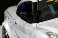 A close-up view of a black racing-style side mirror mounted on a white RC drift car body.