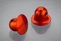 Two orange anodized aluminium RC body shell posts with a rounded top and side hole, displayed on a reflective grey surface.