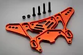 A red anodized aluminium rear shock tower for an RC car, accompanied by four black metal screws and two black nuts, set against a plain grey background.