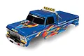 A blue Traxxas Bigfoot RC monster truck body shell with colorful decals, chrome roll bar, and KC light bar, isolated on a white background.
