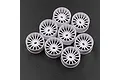 A set of eight white plastic RC car rims with a multi-spoke design arranged on a dark textured surface.