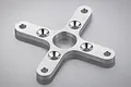 A silver-coloured, X-shaped aluminium motor mount for an RC plane, featuring a central hole and four mounting arms with countersunk screw holes.