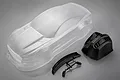An unpainted clear polycarbonate RC car body shell with black plastic accessories including a rear wing and a front bumper piece.