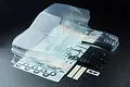 A clear, unpainted MST 1/10 scale E30RB RC car body shell with included decal sheets, plastic parts, and accessories on a black background.