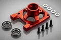 A red anodized aluminium clutch bell brace for RC cars, shown with two ball bearings, four silver washers, and four black hex screws on a grey background.