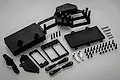 A Rovan dual steering servo tray kit including black plastic mounts, covers, two silver aluminium servo horns, and various screws and clips.