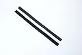 Two thin strips of black adhesive hook and loop fastener material laid diagonally on a white background.