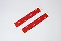 Two strips of red double-sided adhesive tape with 3M branding on the backing, laid diagonally on a white background.