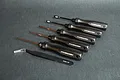 A set of five Koswork screwdrivers and one pair of tweezers arranged on a dark grey surface.