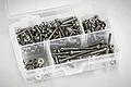 A clear plastic storage box filled with various sizes of stainless steel RC screws and nuts, viewed from above against a white background.