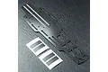 A carbon fibre RC car main chassis plate with two sets of adhesive pads on a textured dark grey surface.