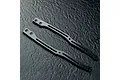 Two carbon fibre RC chassis upper deck components with metal mounting inserts, displayed on a dark textured surface.