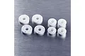 A set of eight white plastic RC shock pistons and spacers arranged on a brushed metal surface.