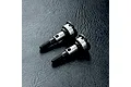 Two MST RC wheel axles made of metal, shown on a black textured surface.