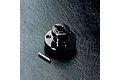A black aluminium spur gear mount for an RC car, shown with a small metal pin on a textured black surface.