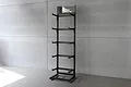 A black Koswork 5-layer metal display stand standing against a grey concrete wall.