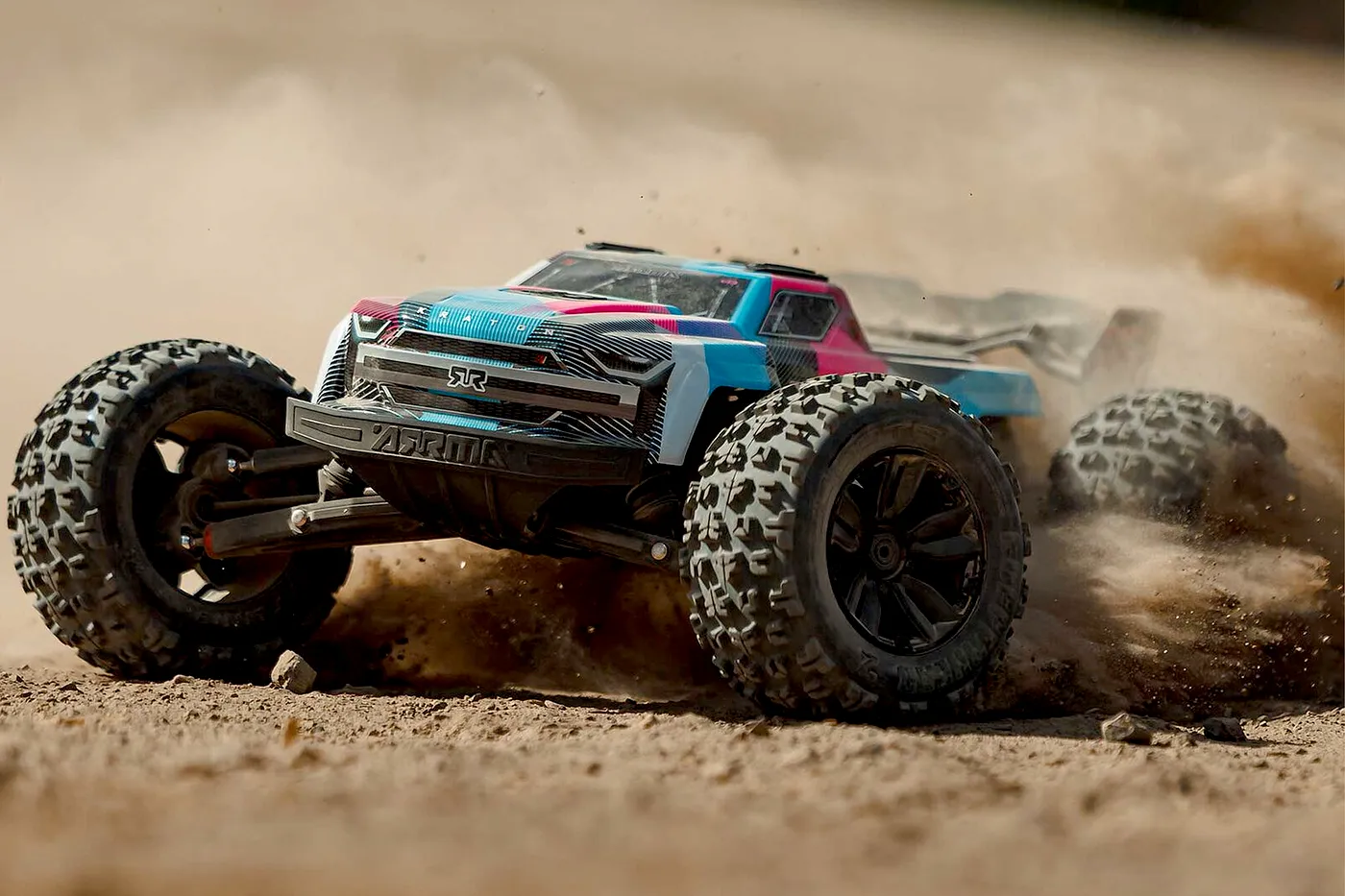 An ARRMA Kraton RC truck driving fast on a dirt track, kicking up a large cloud of dust.