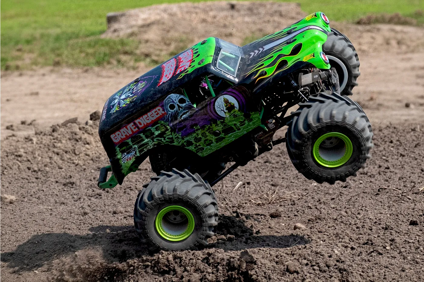 A Grave Digger RC monster truck performing a wheelie on a dirt track outdoors.