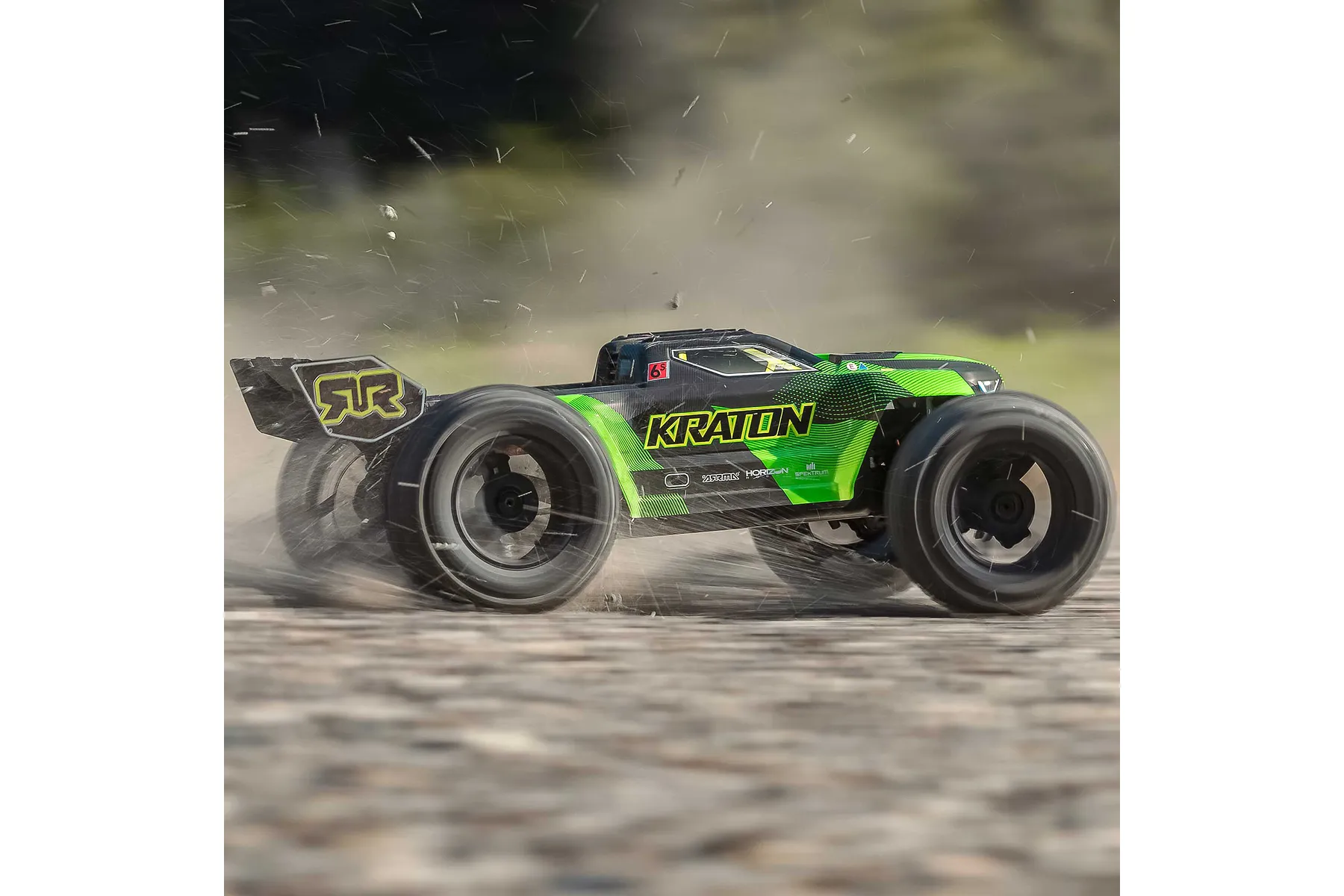 ARRMA Kraton 6S V6 RC truggy in green and black driving fast on a dirt track, kicking up dust and debris.