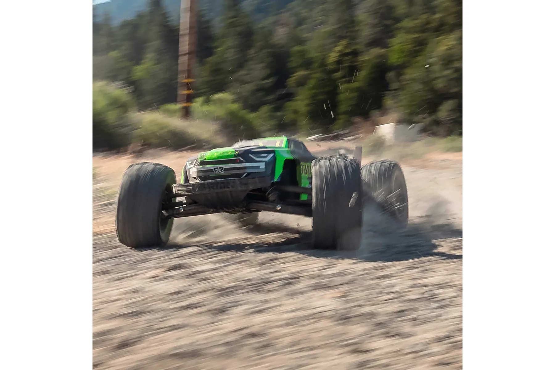 An ARRMA Kraton 6S V6 RC truggy in green and black driving fast on a dirt track, kicking up dust.