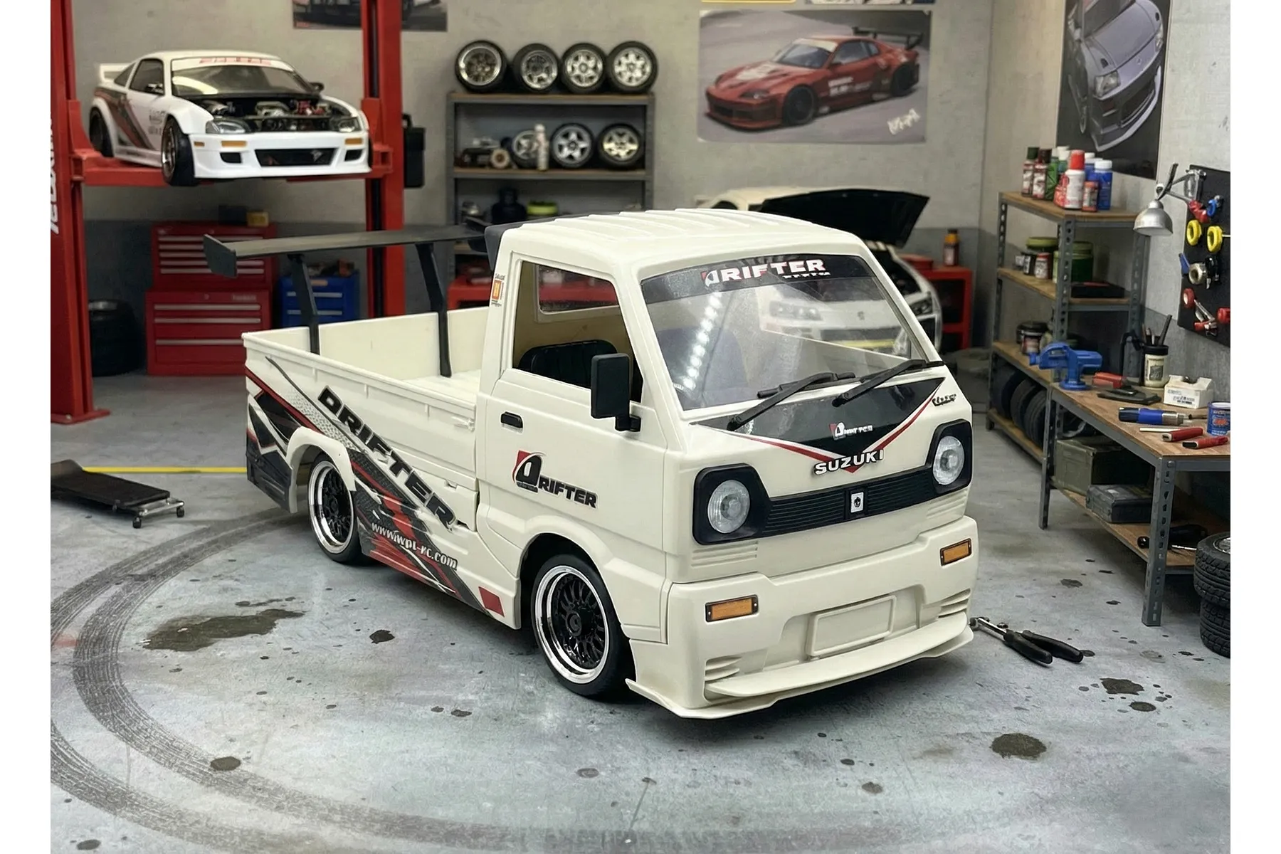 A white WPL D14S Suzuki Carry RC drift truck with wide body kit, parked in a detailed miniature garage diorama.