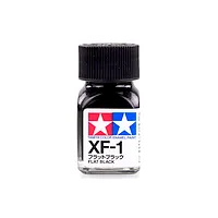 A small glass bottle of Tamiya XF-1 Flat Black enamel paint with a black screw-top lid against a white background.