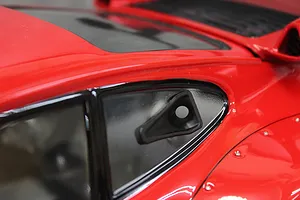 A close-up of a black NACA duct accessory installed on the side window of a red 1/10 scale RC car body.